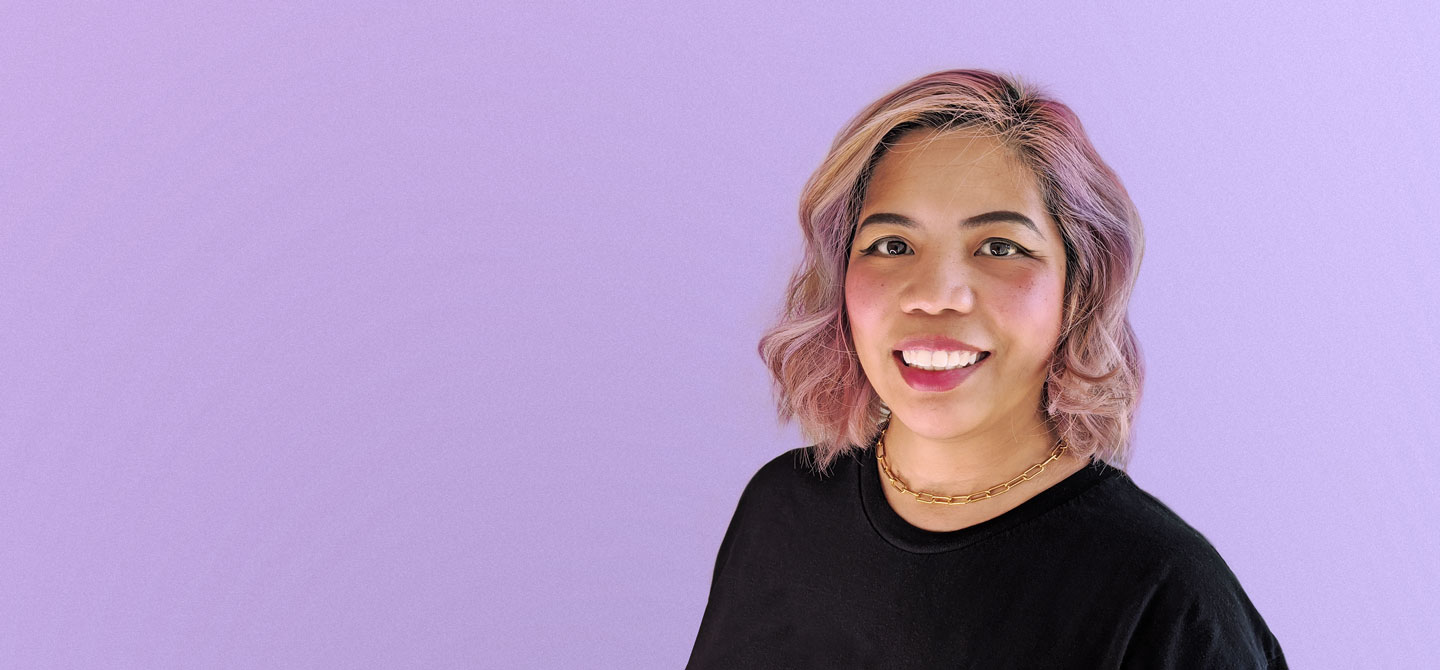 Headshot of Donna Vitan smiling, wearing a plain black t-shirt with a solid lavendar background